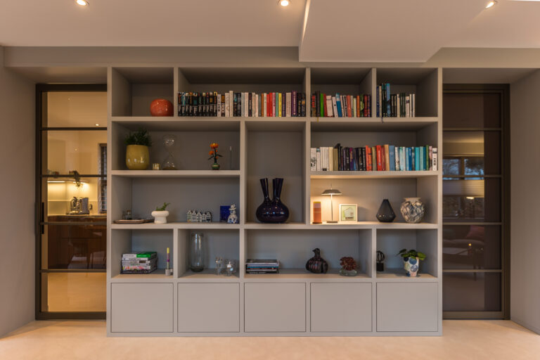 Maatwerk kastwand met open vakken, boeken, decoratieve accessoires en sfeerverlichting als stijlvolle roomdivider in een modern interieur.